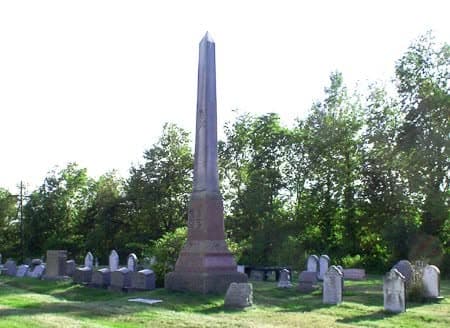 A stone cemetery monument on a green lawn with trees behind it.